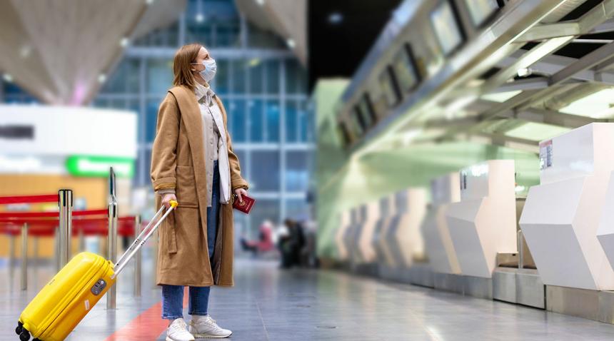 Woman wearing a surgical mask, with luggage at the airport.